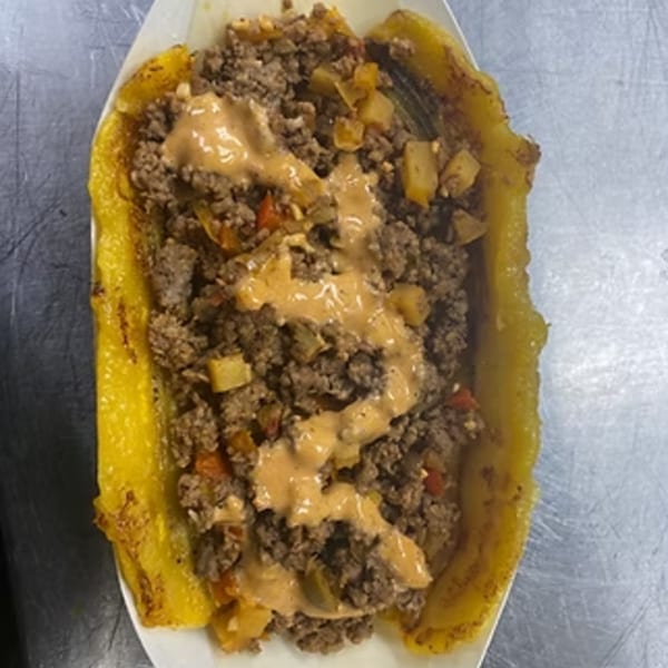 A boat-shaped fried plantain filled with seasoned ground beef, potatoes, and drizzled with sauce.