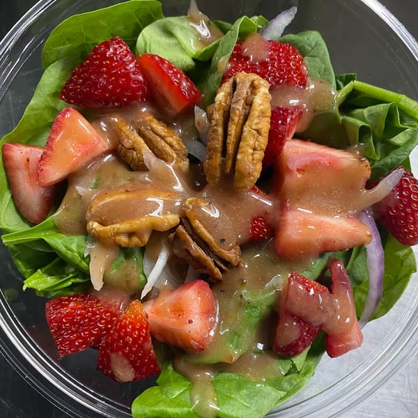 A vibrant spinach salad with sliced strawberries, pecans, red onion, and a vinaigrette dressing.