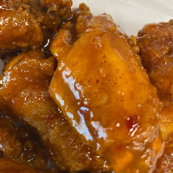 Close-up of several chicken wings coated in a glossy, orange-brown sauce with visible spices.
