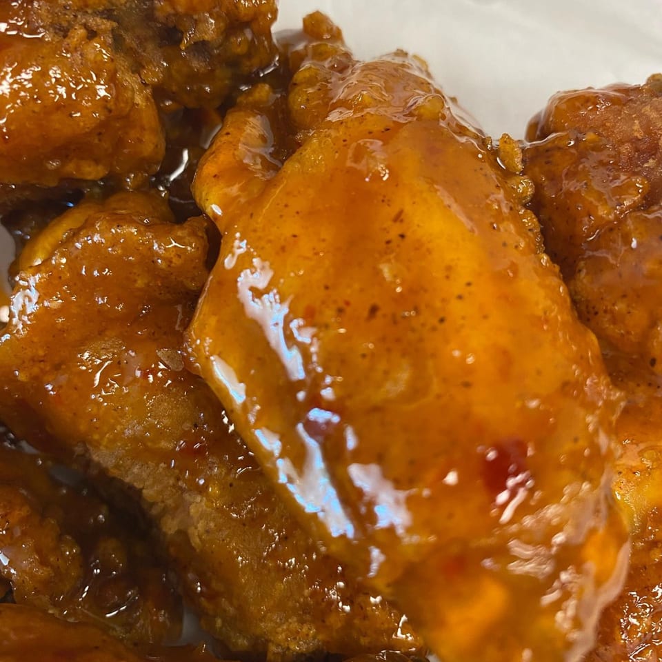 Close-up of several chicken wings coated in a glossy, orange-brown sauce with visible spices.