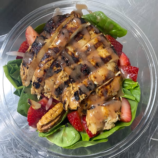 Grilled chicken salad with strawberries, pecans, and spinach in a clear plastic container.