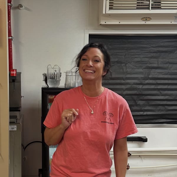 Smiling woman in a red Empanada Grill t-shirt standing in a kitchen setting.