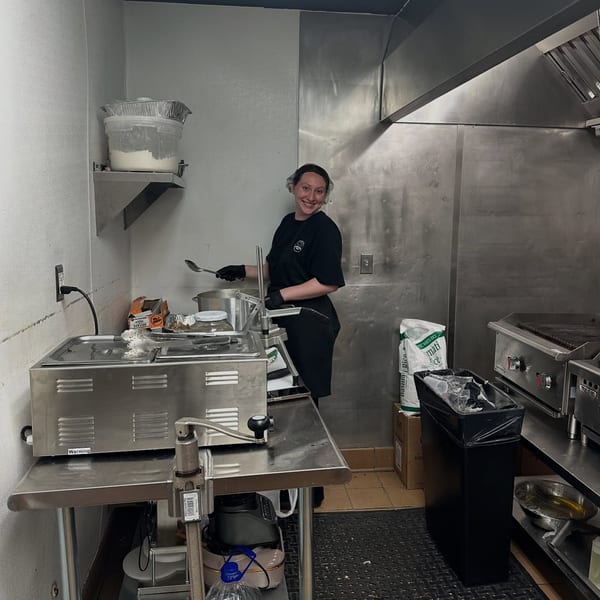An Empanada Grill employee smiles while working in a stainless steel kitchen, preparing food.