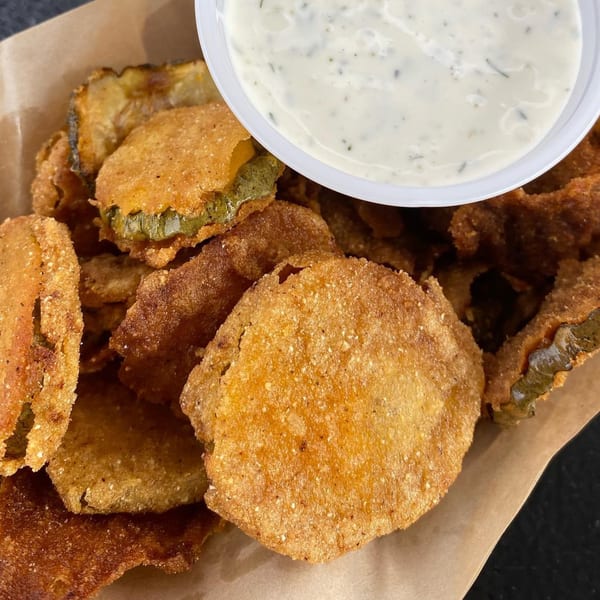 Crispy fried pickles with a side of creamy ranch dipping sauce in a white cup.