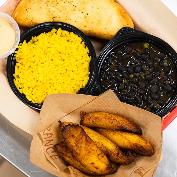 Empanada Grill meal with a large empanada, yellow rice, black beans, fried plantains, and dipping sauce.