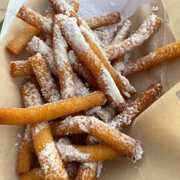 Close-up of golden churro sticks dusted with powdered sugar, served in a brown paper-lined container.