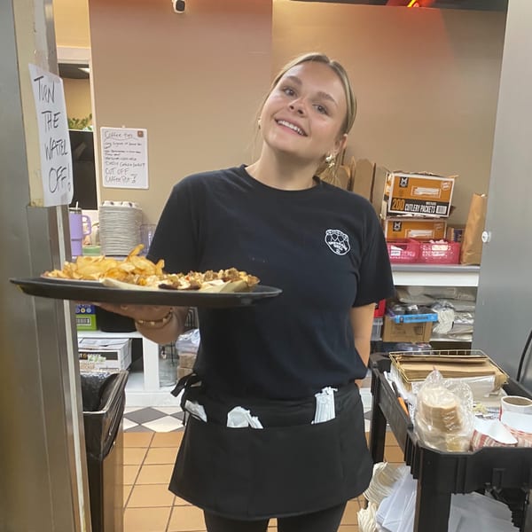 Smiling Empanada Grill employee in a black uniform holding a tray of empanadas and chips.